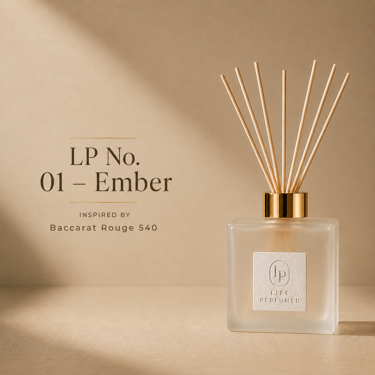 A reed diffuser bottle with light wood reeds and a gold cap on a beige surface, with text reading 'LP No. 01 - Ember' and 'INSPIRED BY Baccarat Rouge 540' on the left.