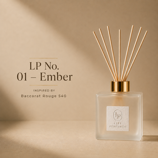 A reed diffuser bottle with light wood reeds and a gold cap on a beige surface, with text reading 'LP No. 01 - Ember' and 'INSPIRED BY Baccarat Rouge 540' on the left.