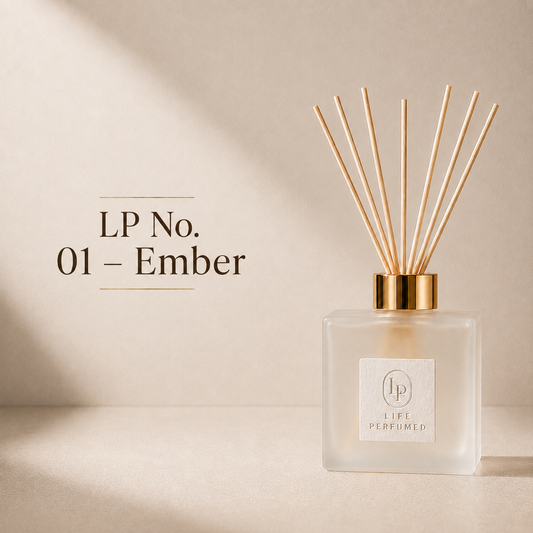 A reed diffuser bottle with natural wood reeds, a gold cap, and a frosted glass body on a warm beige background. Text on the left reads 'LP No. A captivating blend of warm amber, delicate jasmine and rich cedarwood creates an unforgettable fragrance that feels sophisticated, modern and effortlessly luxurious. Smooth, radiant and long-lasting, Ember transforms every home into an elegant escape.