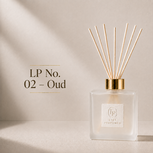 A reed diffuser bottle with a gold cap and natural reeds, shown on a warm beige background with text reading 'LP No. 02 - Oud'. A timeless bouquet of velvety rose petals wrapped in warm amber and soft woods. Rich yet beautifully balanced, Taif fills your car with an elegant floral fragrance that feels refined, luxurious and unforgettable.