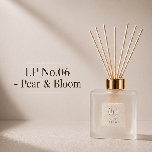 A Life Perfumed LP No.06 reed diffuser in Pear & Bloom scent, featuring a frosted glass bottle with a gold collar and natural wood reeds, set against a warm beige background with elegant text overlay. A beautifully fresh blend of juicy ripe pear, delicate freesia and soft floral notes creates an elegant fragrance that feels bright, feminine and effortlessly refined. Crisp, fresh and inviting, Pear &amp; Bloom brings a touch of understated luxury to your home.