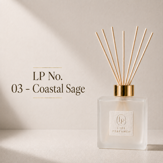 A Life Perfumed reed diffuser bottle made of frosted glass with a gold collar and natural wood reeds, set against a warm beige background with text reading 'LP No. 03 - Coastal Sage'. A refreshing blend of crisp sea salt, aromatic sage and soft woody notes creates an effortlessly sophisticated fragrance that captures the feeling of a cool coastal escape. Fresh, clean and calming, Coastal Sage brings the natural beauty of the ocean and shoreline to your home.